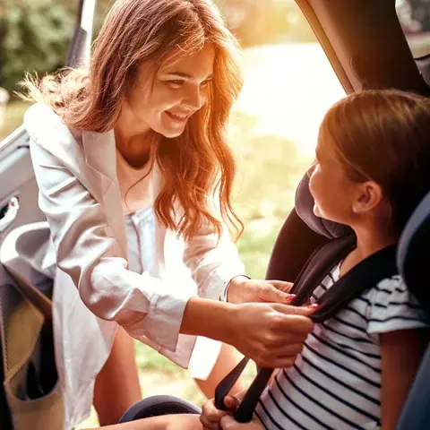 Imagem de uma mãe, cliente Pattini Seguros, colocando o cinto de segurança na sua filha. Seguro Auto Allianz