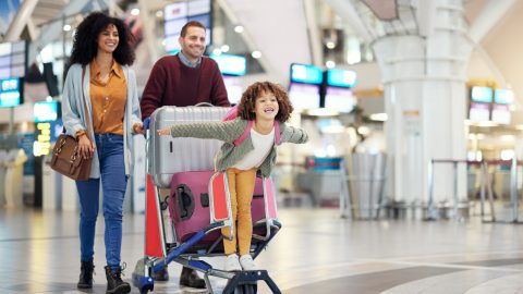 Família em um aeroporto, casal e filho em um carrinho de viagem, felizes com a proximidade de uma viagem segura, com seguro viagem da Pattini Seguros