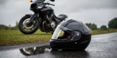 Capacete preto no chão molhado com moto ao fundo, representando a proteção de acessórios como capacete, jaquetas, luvas e intercomunicador no seguro moto