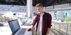 Jovem avaliando notebooks em uma loja de eletrônicos, simbolizando indenização financeira prevista na cobertura seguro notebook e tablet