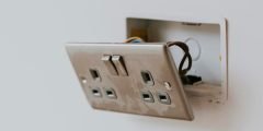 Tomada danificada com fios expostos em parede residencial, representando risco elétrico coberto pelo seguro