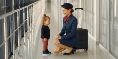 Criança pequena interagindo com comissária de bordo em aeroporto, ilustrando a cobertura seguro viagem para acompanhamento de menor e hospedagem de acompanhante.