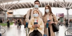Família usando máscaras em aeroporto com passaportes nas mãos, demonstrando a cobertura seguro viagem para COVID-19, esportes e perda de documentos.