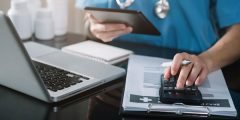 Profissional da saúde usando calculadora entre laptop e documentos, ilustrando a cobertura seguro viagem para reembolso de despesas médicas.