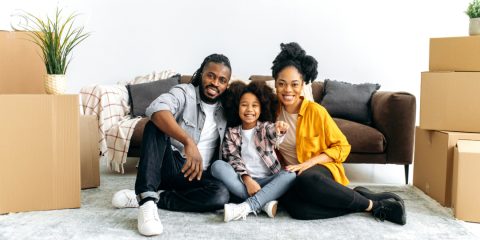 Família feliz sentada no chão da nova casa com caixas de mudança ao redor, representando a conquista do imóvel próprio por meio de consórcio imobiliário planejado, sem entrada e sem juros.