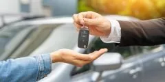 Pessoa entrega a chave de um carro para outra, em frente a um veículo estacionado. A cena representa a cobertura de carro reserva do seguro auto Pattini, que garante um veículo substituto ao segurado durante o período em que o carro principal estiver em reparo por conta de um sinistro.