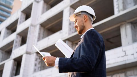 Engenheiro usando capacete branco e analisando documentos técnicos em frente a um edifício em construção, simbolizando a importância da responsabilidade civil em obras e atividades empresariais.