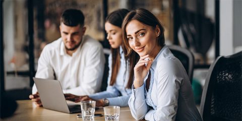 Três profissionais em ambiente corporativo, com foco em uma mulher sorrindo para a câmera, representando segurança, cuidado e valorização dos times com o Seguro Vida Empresarial da Pattini.